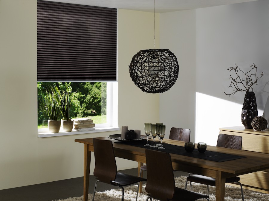 A dining room table next to a window with motorized shades. 