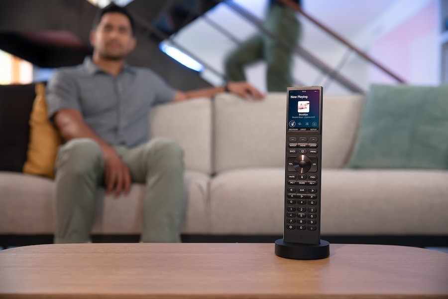 A man sitting on the couch in the background with a Control4 remote on the coffee table in the foreground.