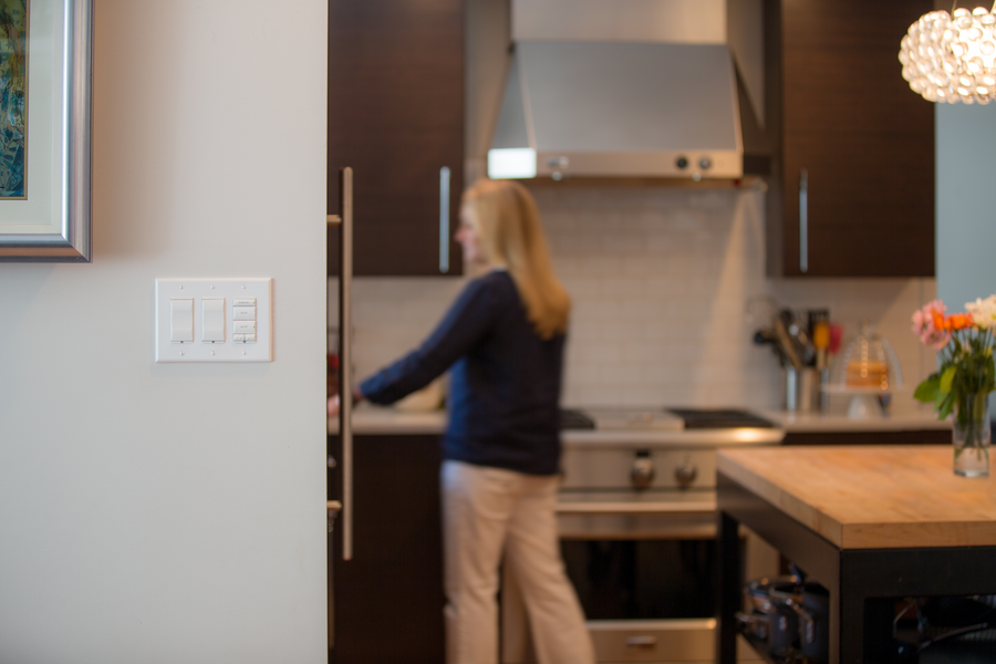 A woman working in the kitchen with Control4 controls on the wall.