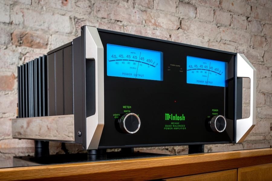 McIntosh MC462 power amplifier with glowing blue watt meters and green logo, set against a rustic brick wall backdrop.